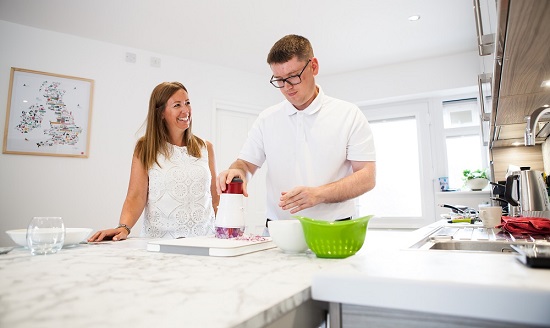 A man using a food processor in a kitchen, guided by an occupational therapist.