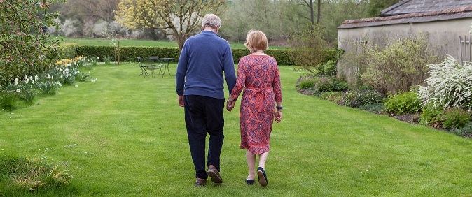 Photo from behind of a couple walking hand in hand in a garden